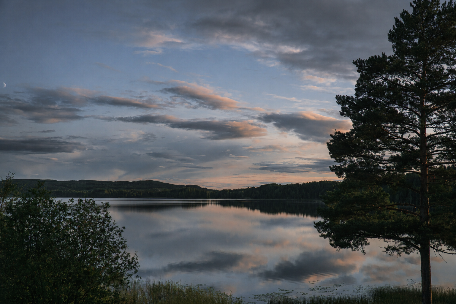 Lago ao crepúsculo, com o céu e as nuvens reflectidos na água calma e pinheiros em silhueta