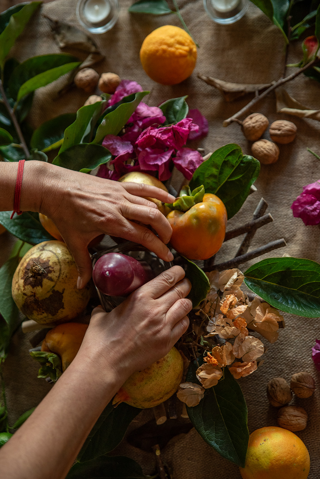 Mãos a compor um centro de frutos, folhas e flores sobre um pano de linho