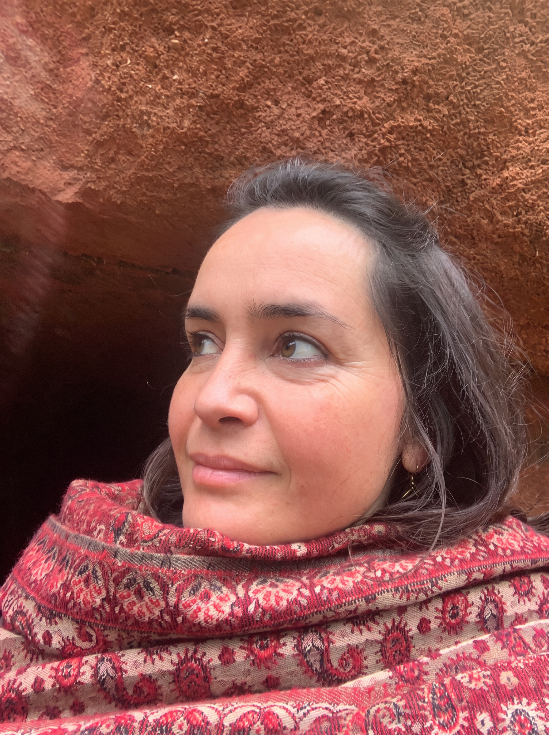 Retrato de Daniela Velho, envolta num xaile de padrão vermelho, junto a uma rocha de tom terra