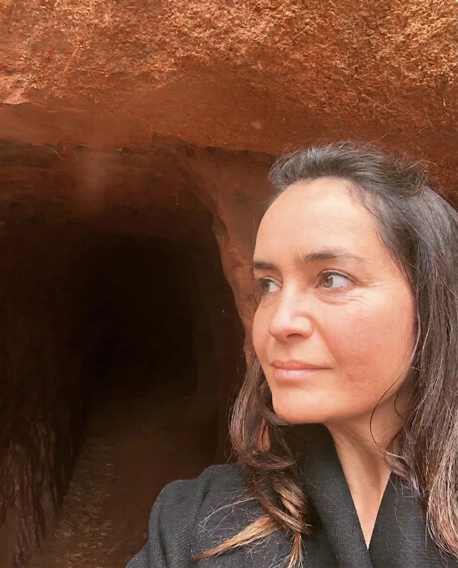 Retrato de Daniela Velho junto a uma gruta de terra ocre, com olhar sereno