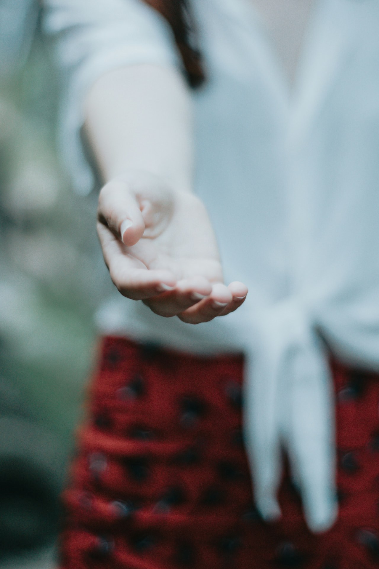 Mão aberta e estendida, de palma voltada para cima, diante de uma camisa clara e de uma saia vermelha